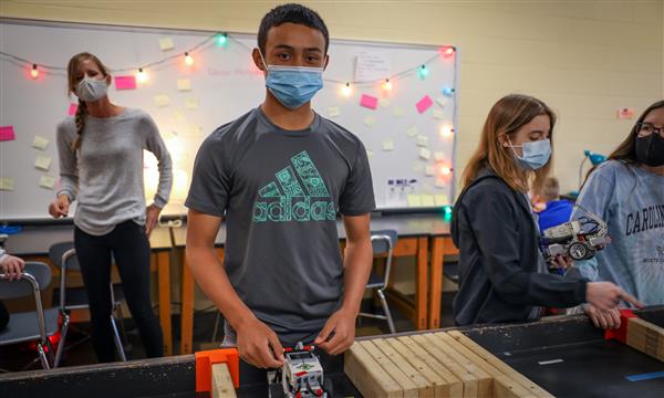 Student smiles at camera while holding robot